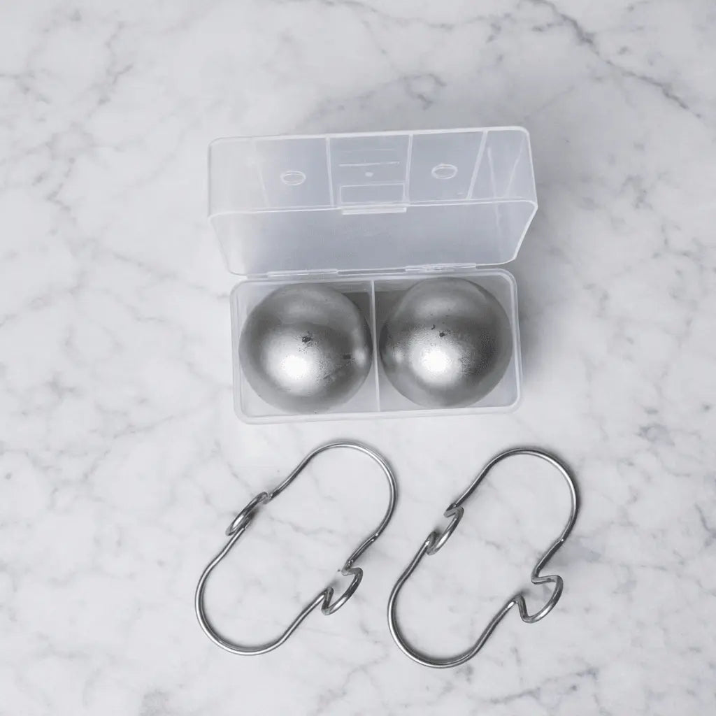 Two large stainless steel espresso cooling balls with hooks and a freezer container from G & J's Finest, used for chilling coffee cups.