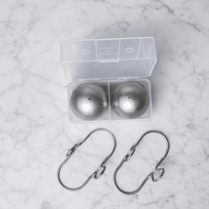 Two large stainless steel espresso cooling balls with hooks and a freezer container from G & J's Finest, used for chilling coffee cups.