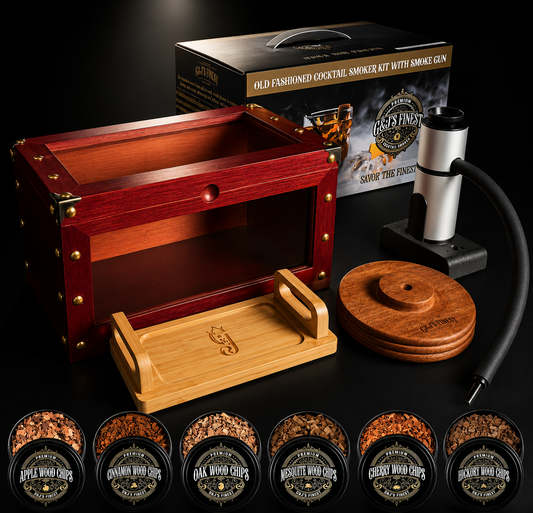 A boxed smoking accessory set displayed on a black background, including a reddish-brown wooden box with brass corner hardware, a bamboo tray, a silver and black pump device, a round wooden lid, and several small jars of wood chips. The packaging box reads 'Old Fashioned Cocktail Smoker Kit with Amok Gen' and 'Savor The Experience.